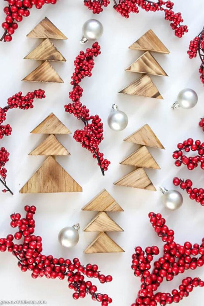 Scrap wood triangles put together as Christmas trees laying with red berry twigs and silver ornaments