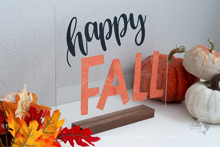 Happy Fall sign on a white table with other fall decorations.