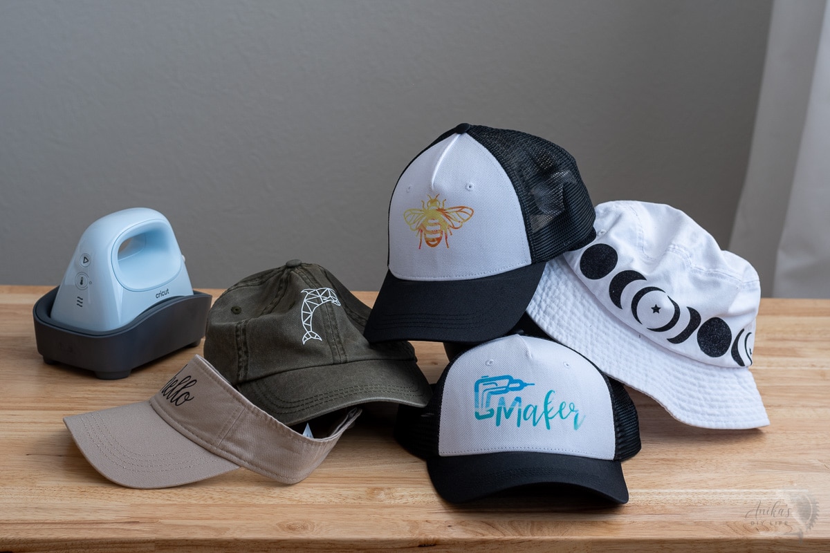 various types of hats with heat transfer designs on table with hat press in the background