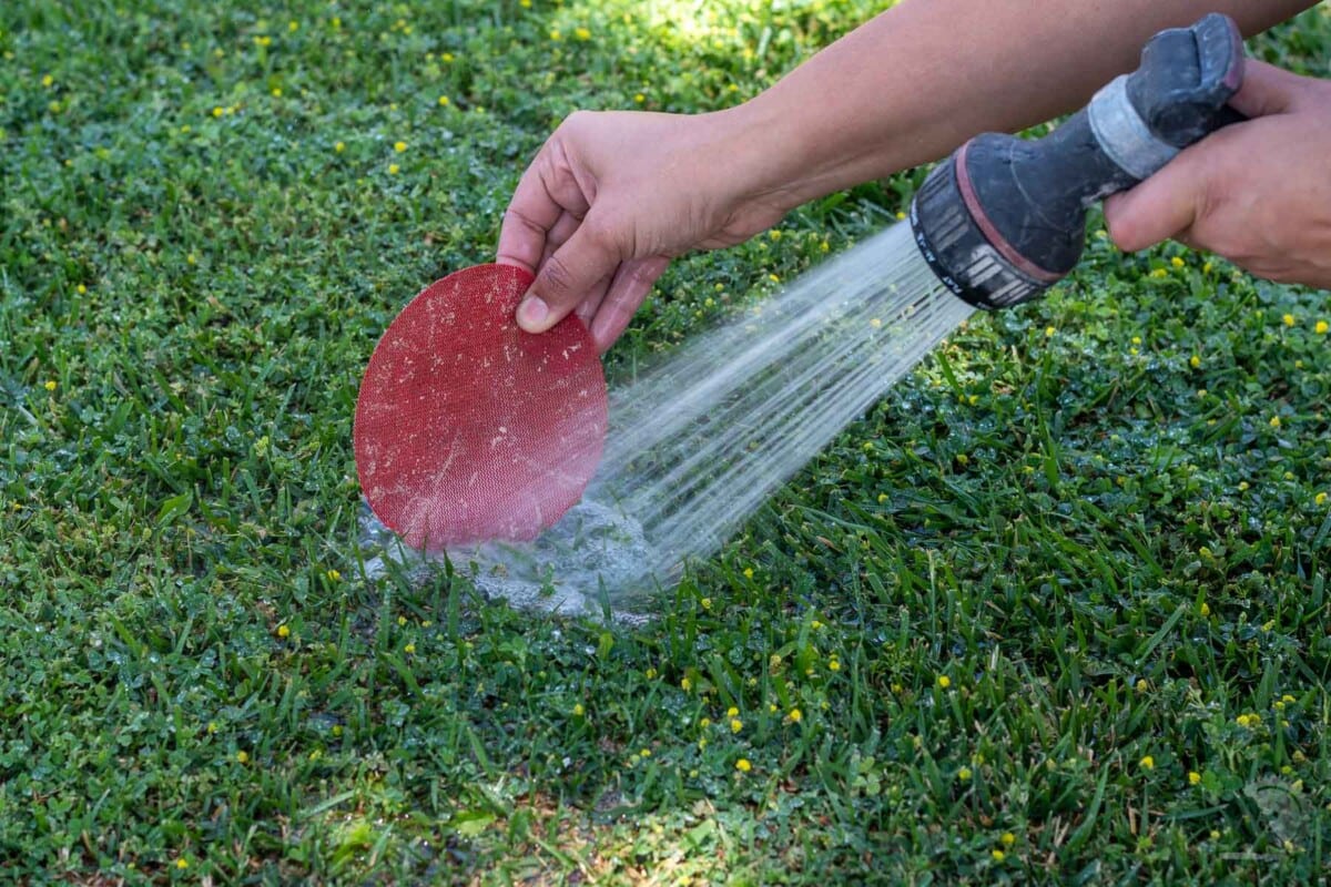 washing a dirty sanding sheet in the grass with a hose.