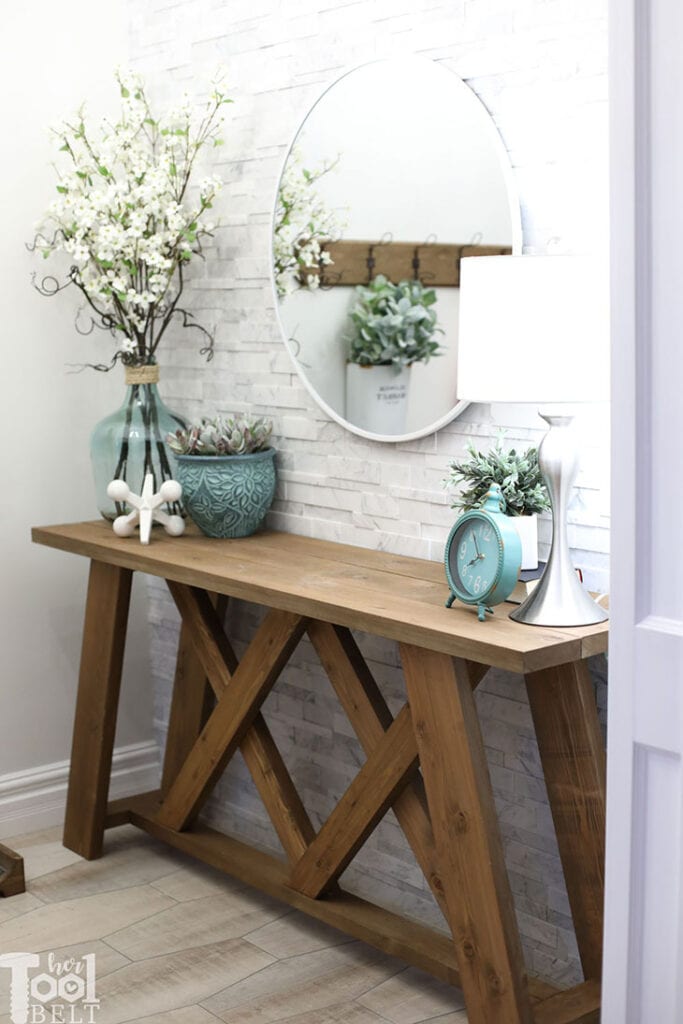 Wooden console table with X design detail against a white tiled wall with mirror above