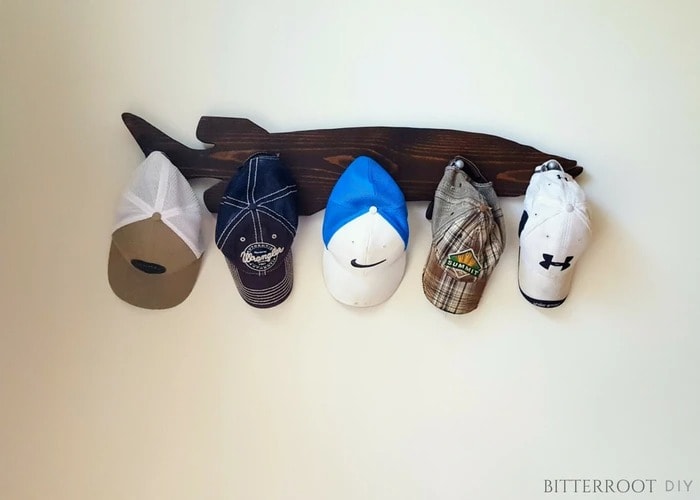 DIY hat rack made from scrap wood in the shape of a fish with baseball hats hanging on it.
