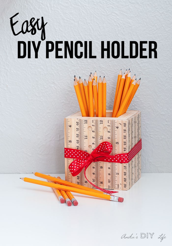 DIY wooden pencil holder with rulers and red ribbon on a white table with yellow pencils inside