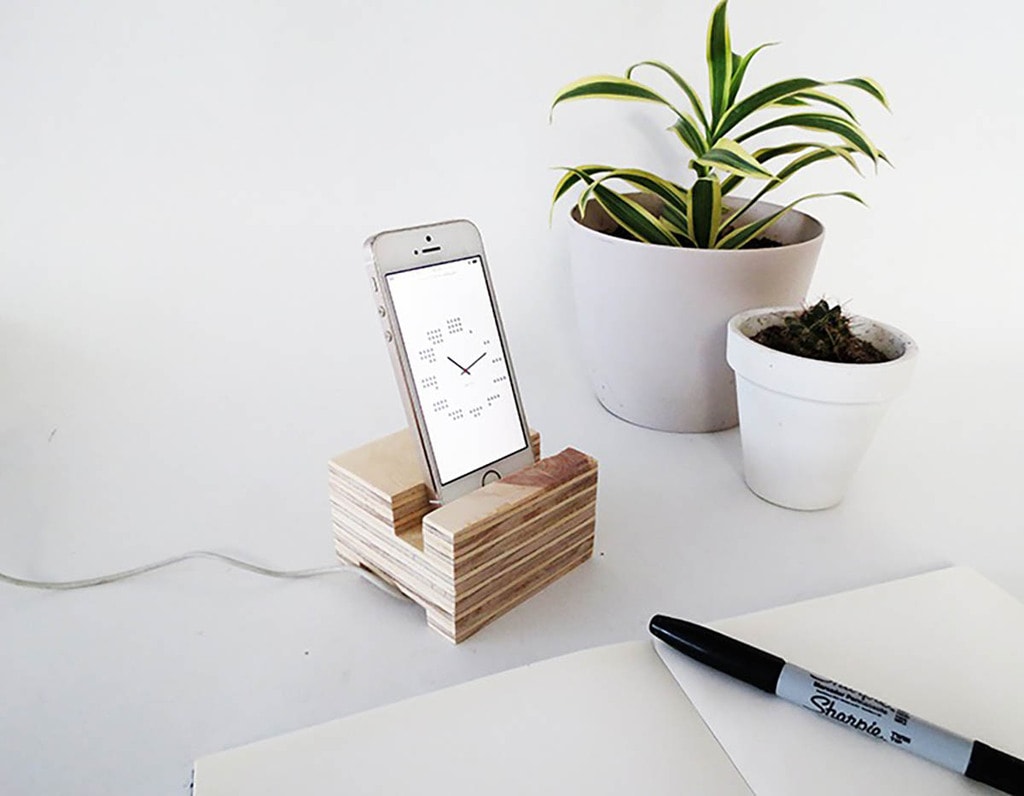 scrap plywood phone holder with iPhone sitting next to pen and notebook