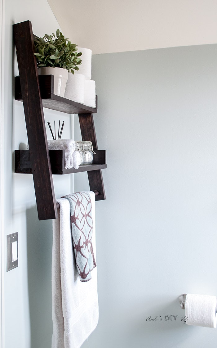 Floating ladder shelf mounted on bathroom wall with flower pot, towels and toileteries