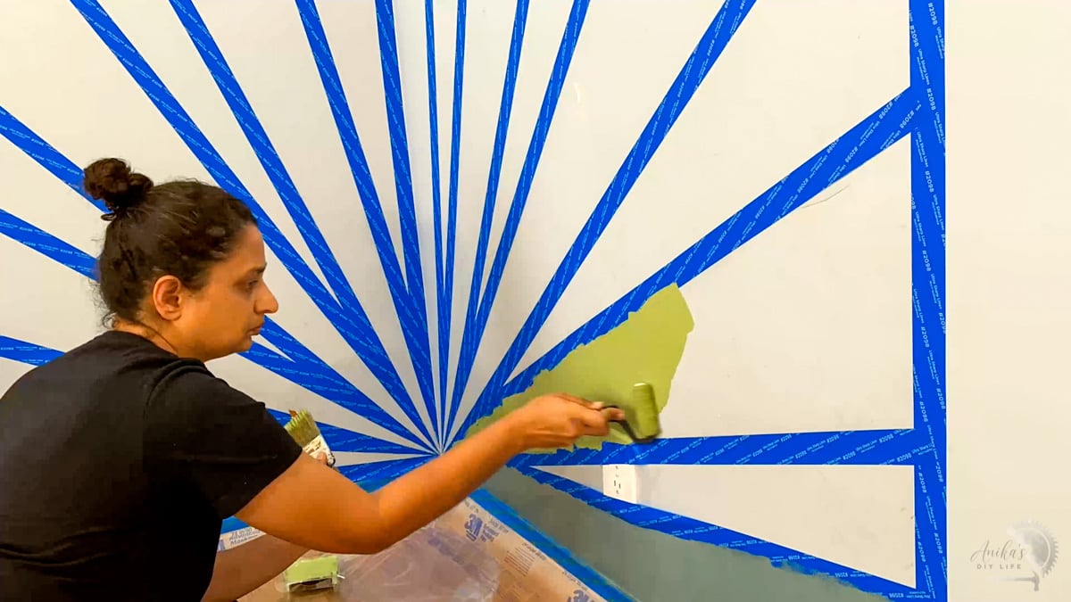 Woman painting stripes in sunburst accent wall.