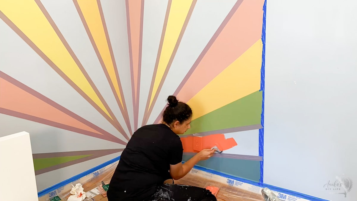 Woman painting red color on wall for sunburst rainbow accent wall