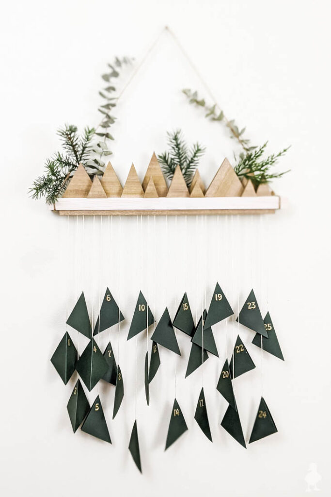 small wood triangle trees on shelf with hanging advent calendar hanging from it