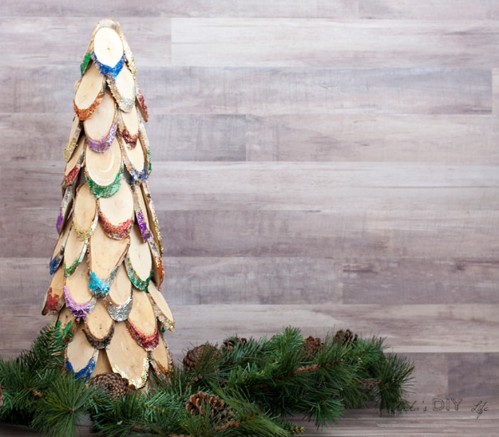 Colorful wood slice christmas tree with greenery on brown background