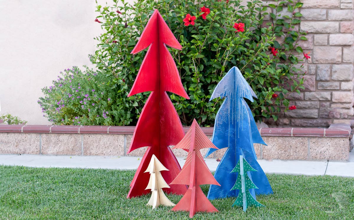 DIY wood Christmas trees standing up in a yard.
