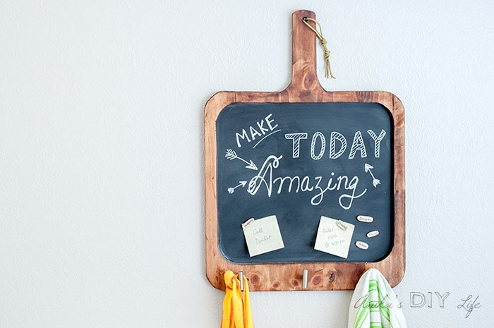 Magnetic chalkboard shaped like a cutting board on wall with note and towel hanging.