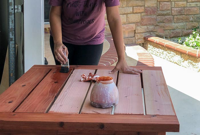Staining the DIY outdoor table with redwood stain