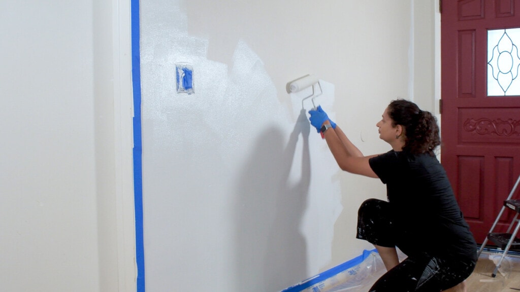 Woman painting a wall white with a paint roller 