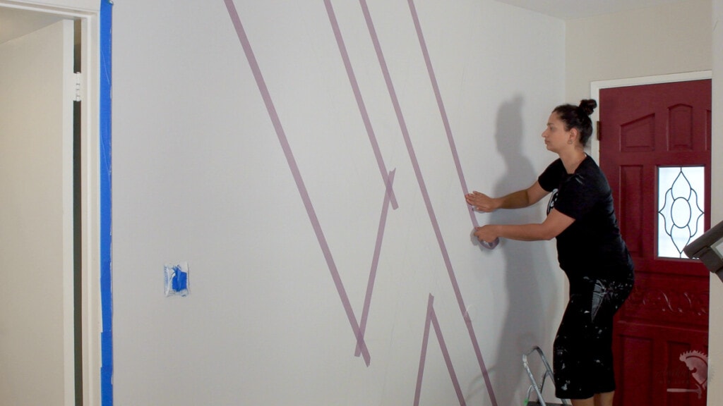 Woman applying tape on the wall to make a concrete accent wall