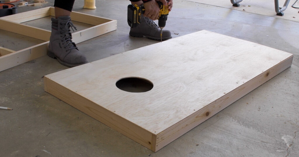 Woman attaching plywood to the frame to build the cornhole board