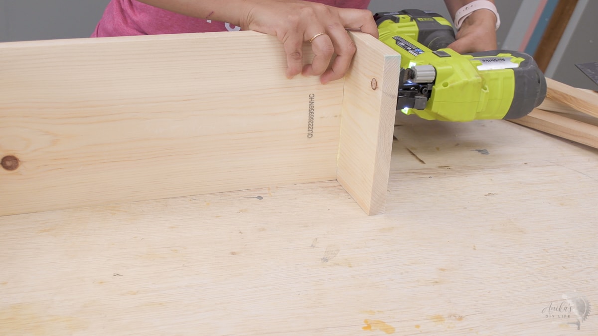 Woman attaching board using a nail gun to make a diy wooden tool box