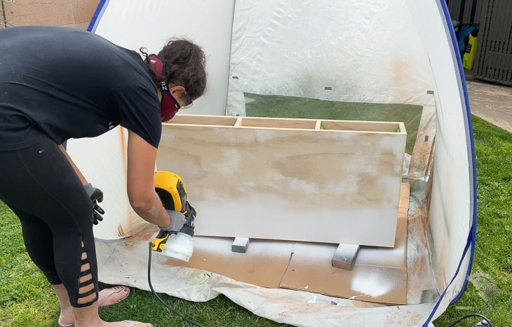 woman applying primer on plywood using a paint sprayer