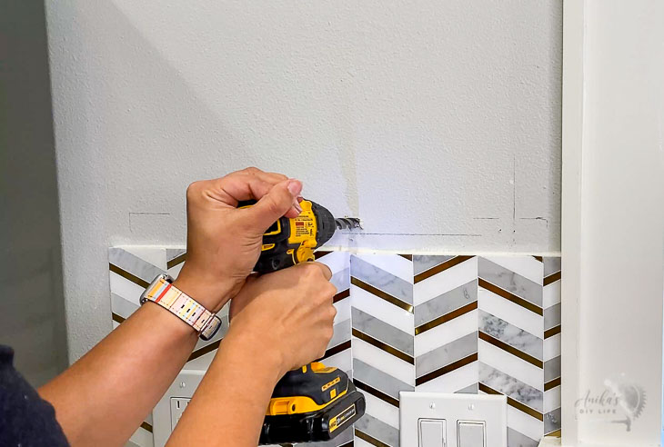 woman making hole in wall with drill bit to install toggle bolts