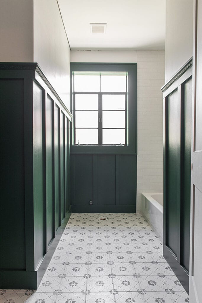 Dark green board and batten wall in a white bathroom with decorative trim detail on top