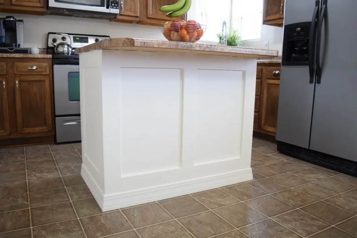 small white island with trim molding and basket of fruit sitting on the countertop