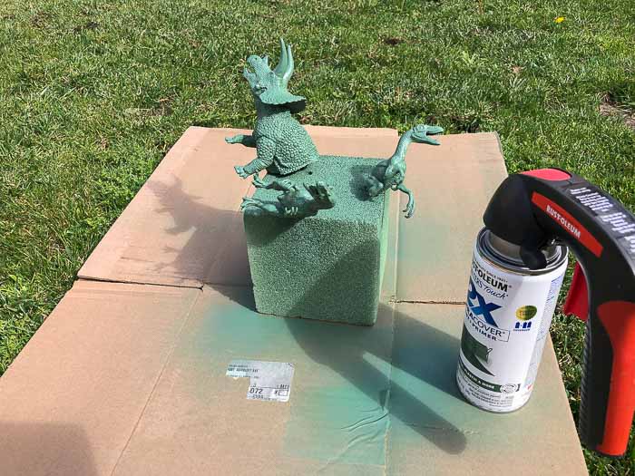 Spray painting dinosaurs green outdoors for the DIY Dinosaur shelf