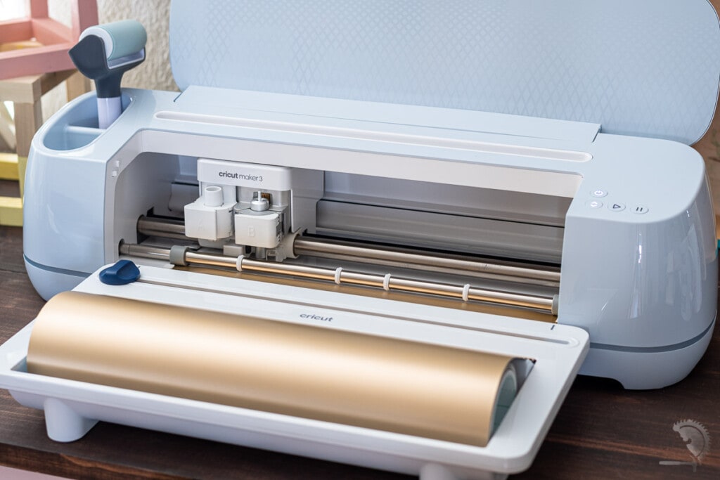 Cricut Maker 3 with roll holder loaded with gold vinyl.